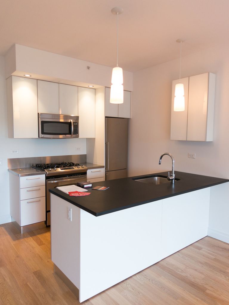 A white modern kitchen with an island, black worktop and glass pendant lights